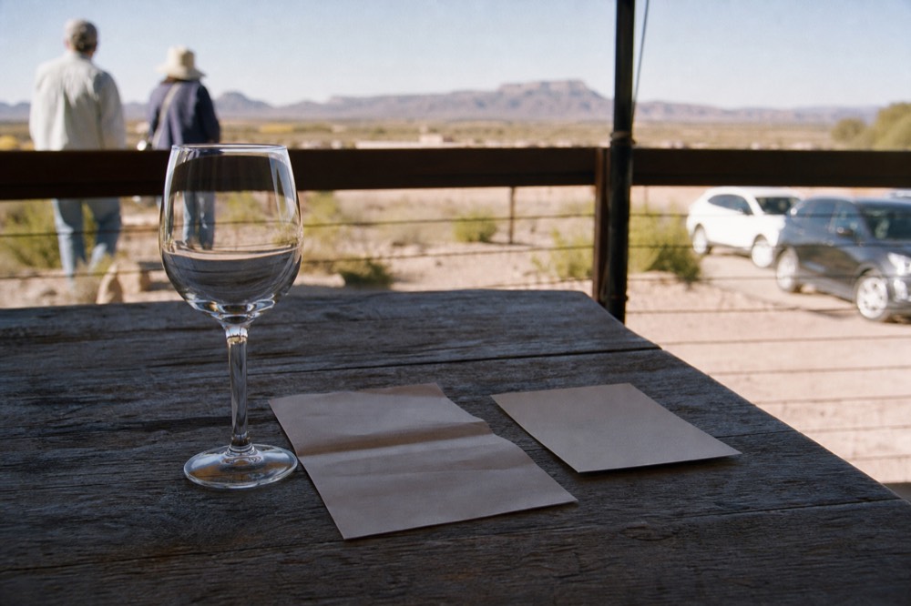 A folded paper tasting list and a printed price card resting beside an empty stemmed glass on a weathered outdoor table