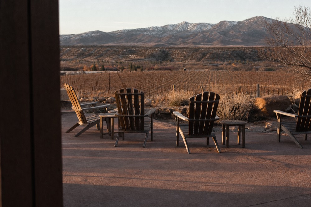 An empty tasting terrace with wooden chairs facing a valley of vines in late afternoon light