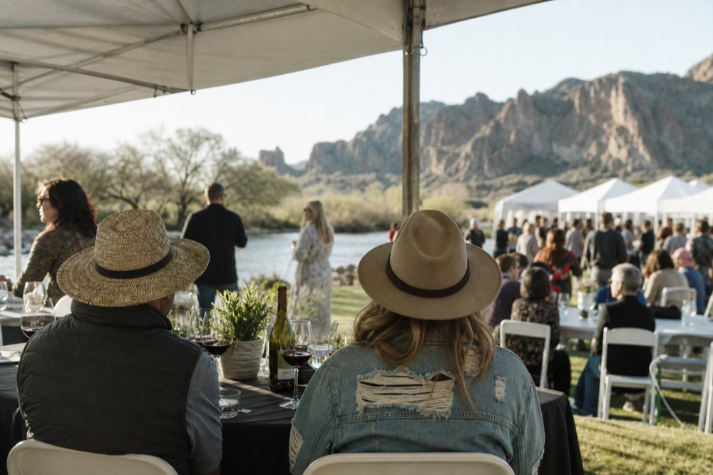 Outdoor wine festival tables under white canopies in a riverside park with crowds holding tasting glasses on a spring afternoon