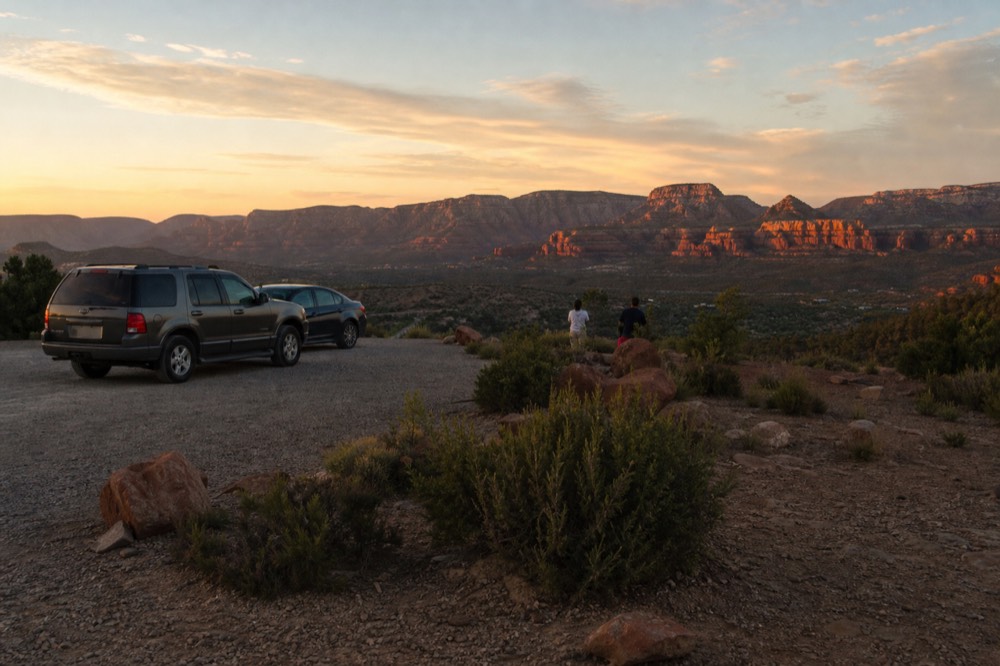 A quiet gravel overlook above a wide desert valley at sunset with layered red rock ridges catching the last light