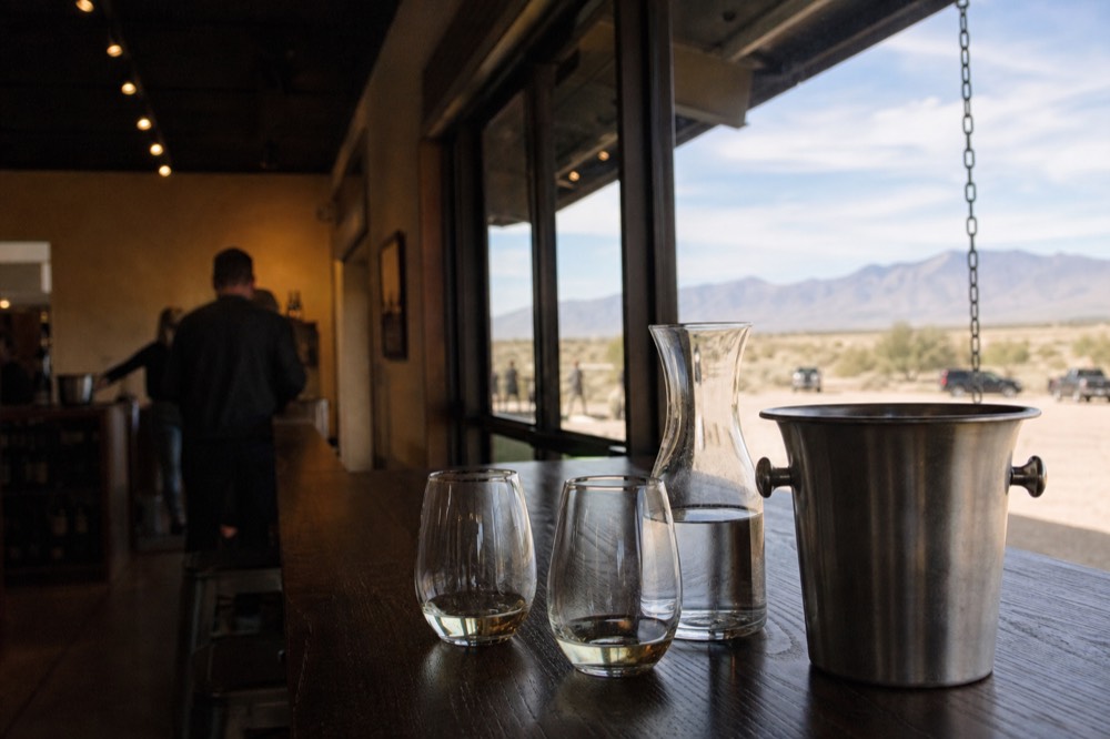 A metal spit bucket and a carafe of water at the end of a tasting bar beside two half-full glasses