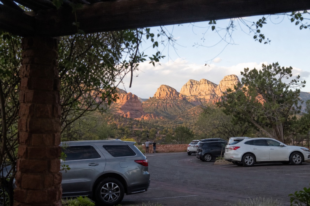 Red sandstone buttes glowing at late afternoon in Sedona with a paved overlook and parked cars in the foreground
