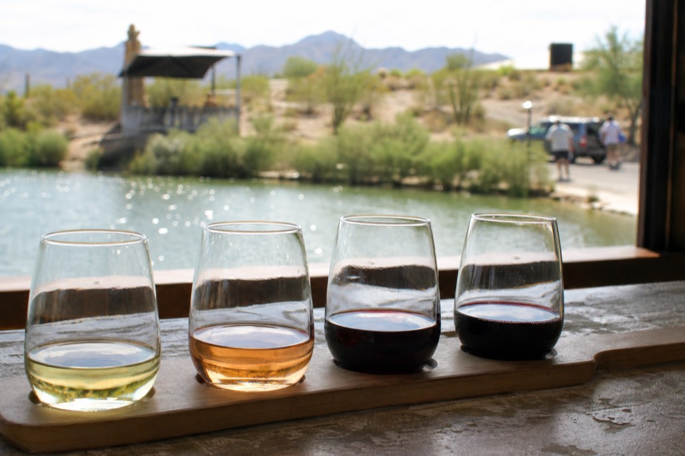 A row of tasting glasses holding four different wines from pale straw to deep purple on a bar top