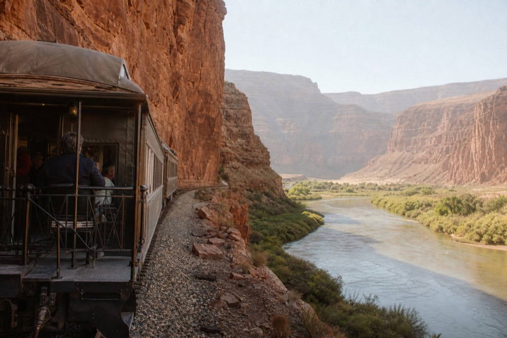 Vintage railroad passenger car with open observation platform stopped beside red canyon walls and a green river below