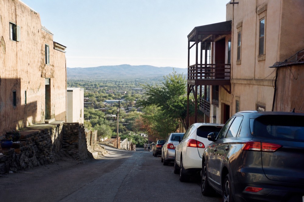 Cars parked at an angle on a steeply pitched narrow street between old buildings, with a valley view opening at the end of the road