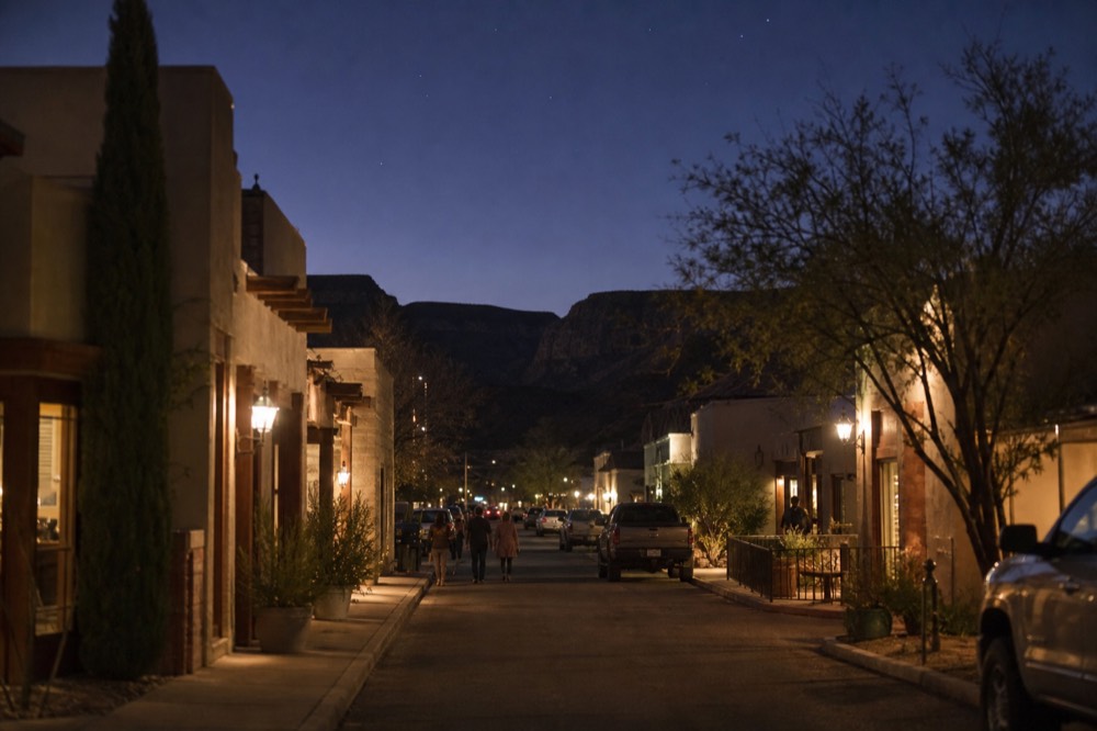 Looking down a straight small-town street with tasting room doorways on both sides and low desert hills closing the view at the end