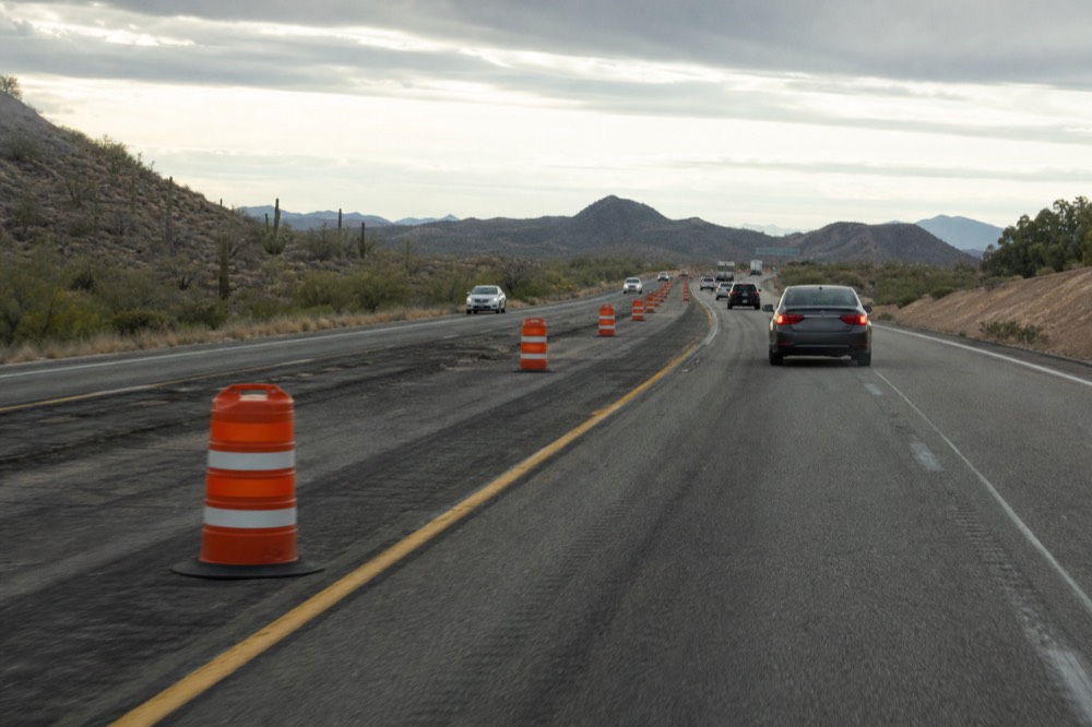 Orange highway construction barrels narrowing a desert freeway to one lane under an overcast late-day sky