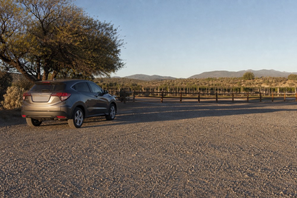 A quiet gravel car park at a small winery in low evening light, one vehicle remaining, vine rows and a wooden fence stretching into shadow